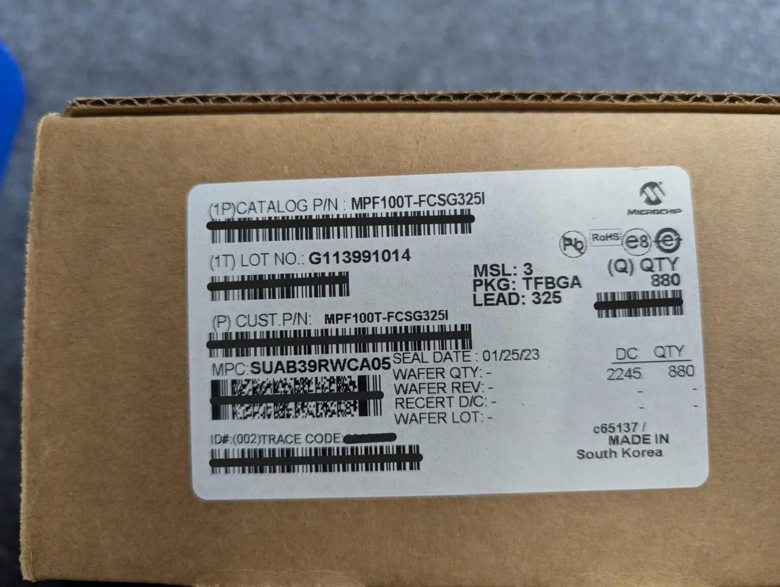 Cardboard box with a white Microchip label reading MPF100T-FCSG325I, package TFBGA, quantity 880, made in South Korea