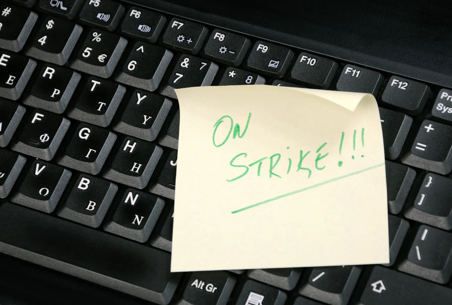 Black keyboard with a yellow sticky note reading ON STRIKE!!! in green handwriting