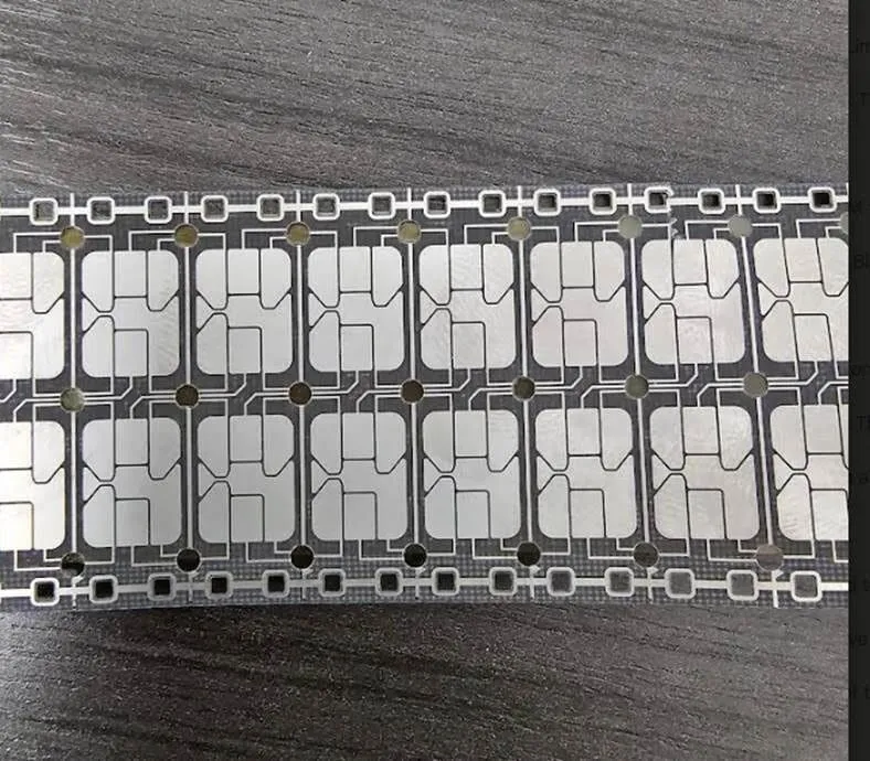 Strip of gray contact-pad modules in two rows on a dark carrier film, lying on a wood-grain surface