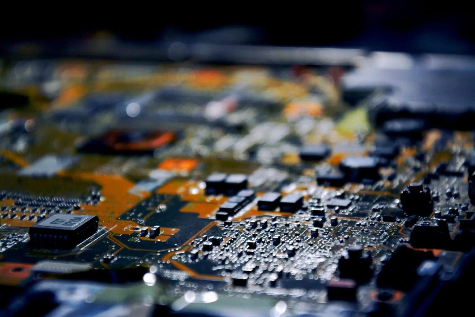 Blurred close-up of a circuit board with small black chips and components in dark, orange-tinted light