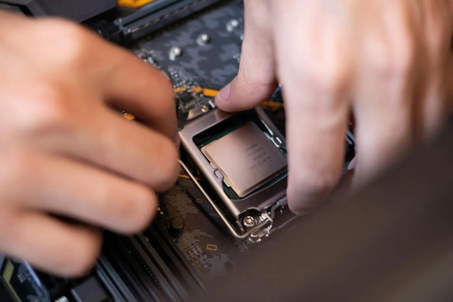 Two hands seating a processor chip into its metal-framed socket on a motherboard