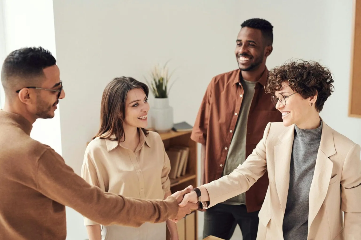 Four smiling people in a bright office, two of them shaking hands while the others look on