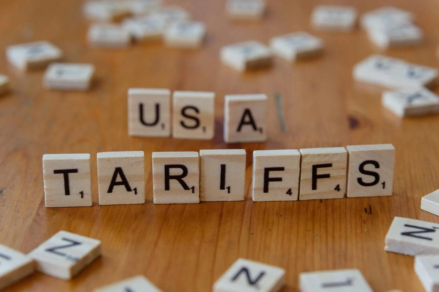 Wooden letter tiles spelling USA TARIFFS on a wooden table with scattered tiles blurred around them