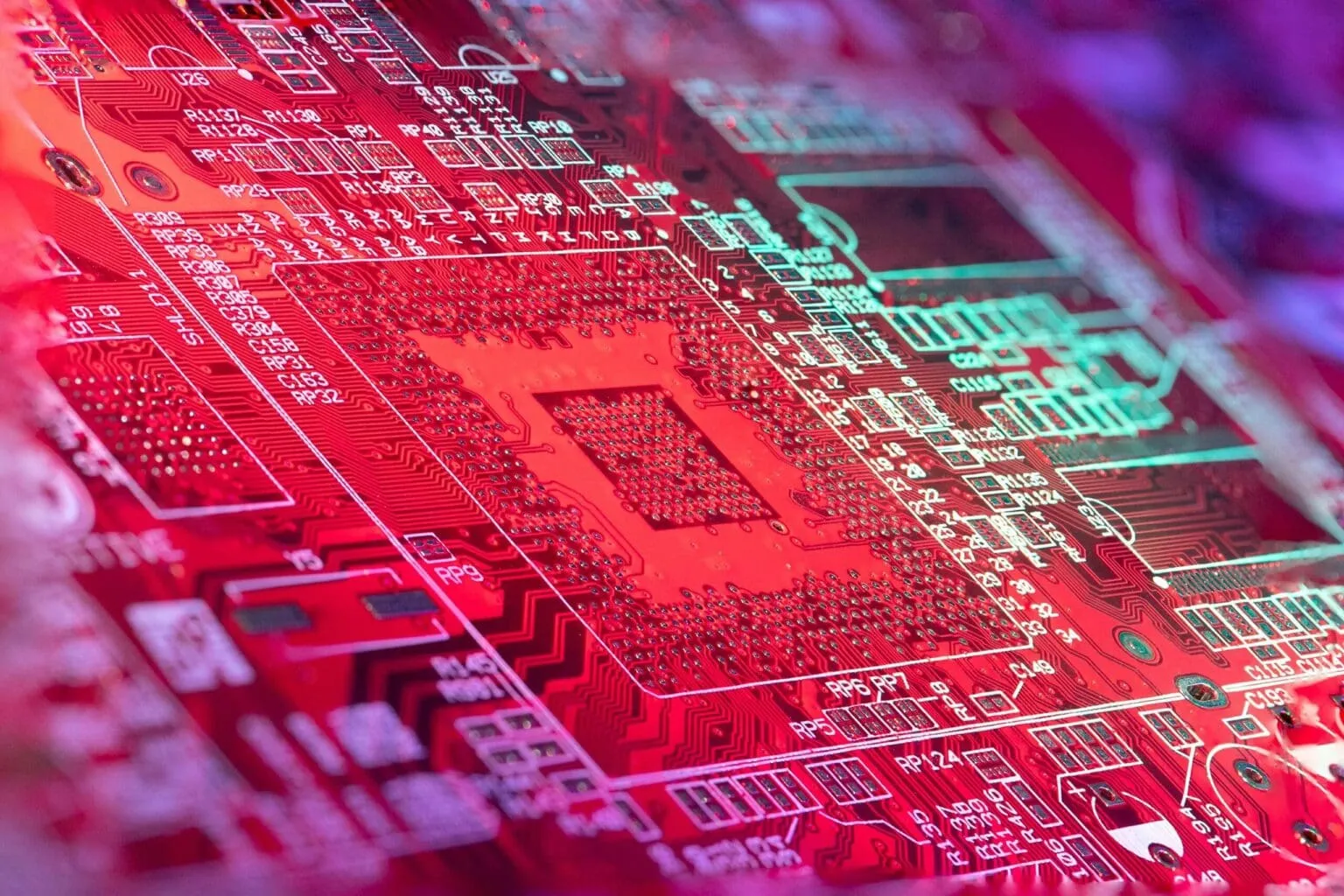 Close-up of a red printed circuit board with white silkscreen part labels and a dense grid of solder pads