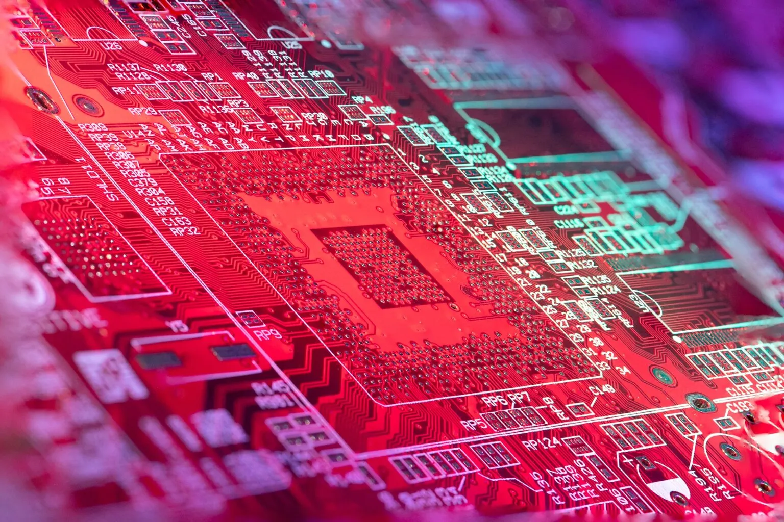 Close-up of a printed circuit board lit red, with white component labels and a large grid of solder pads