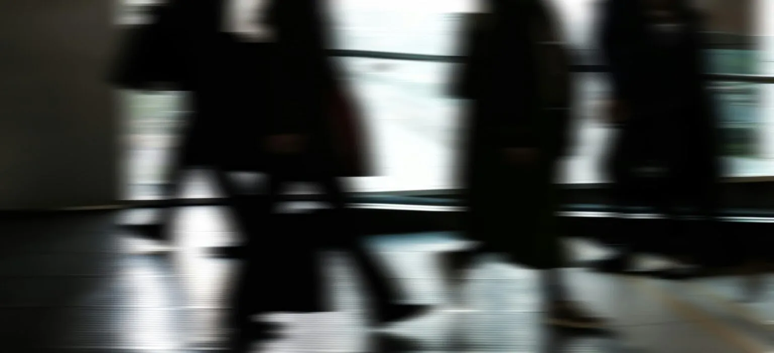 Motion-blurred dark silhouettes of people walking past a bright window