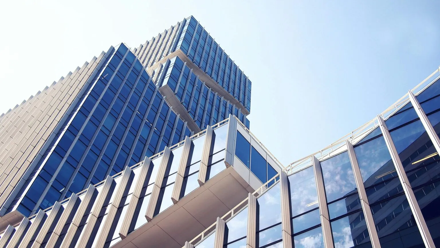 Looking up at a tall glass-and-steel office tower with blue windows against a pale sky