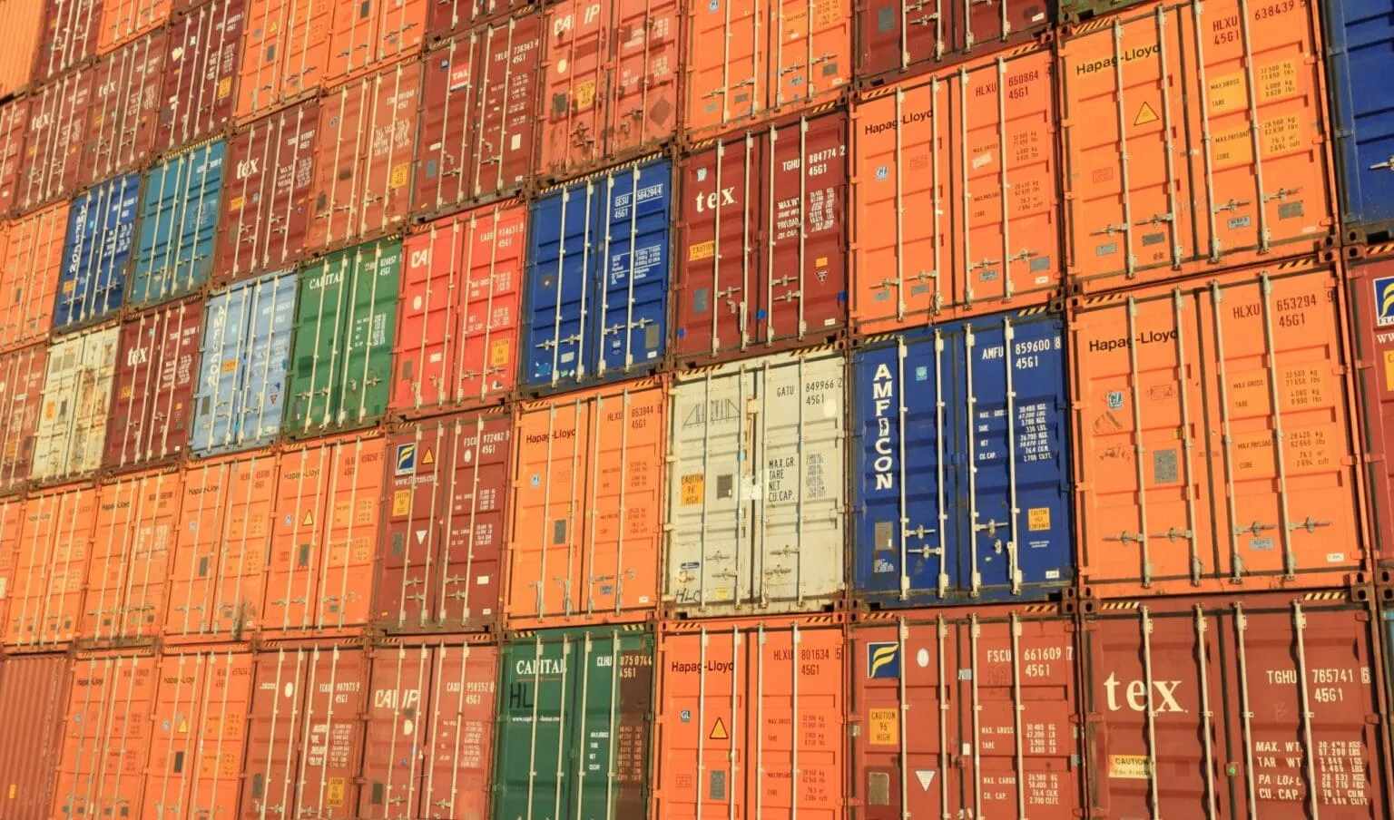 Wall of stacked orange, red, blue and green shipping containers with their doors facing the camera