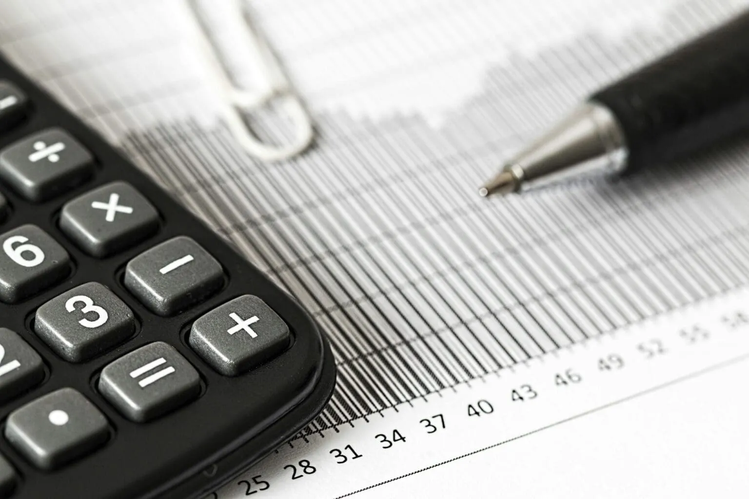 Close-up of a black calculator beside a pen and a printed bar chart with numbered axis