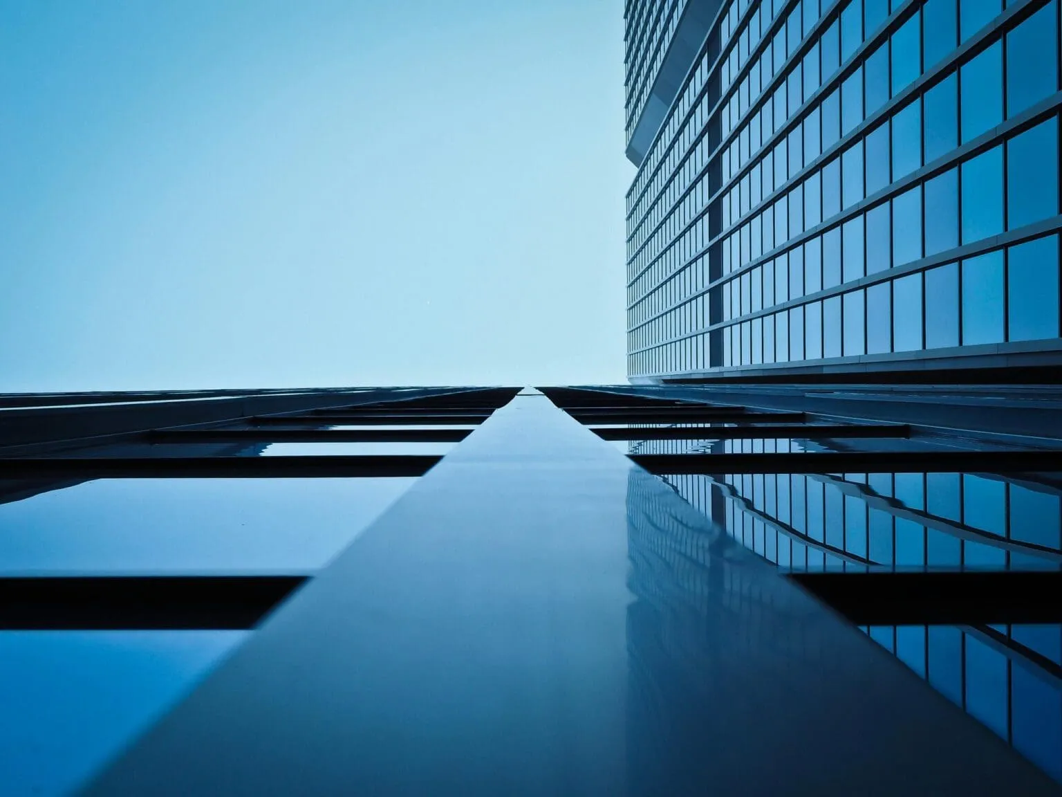 Looking up the glass facade of a tall office tower against a pale blue sky