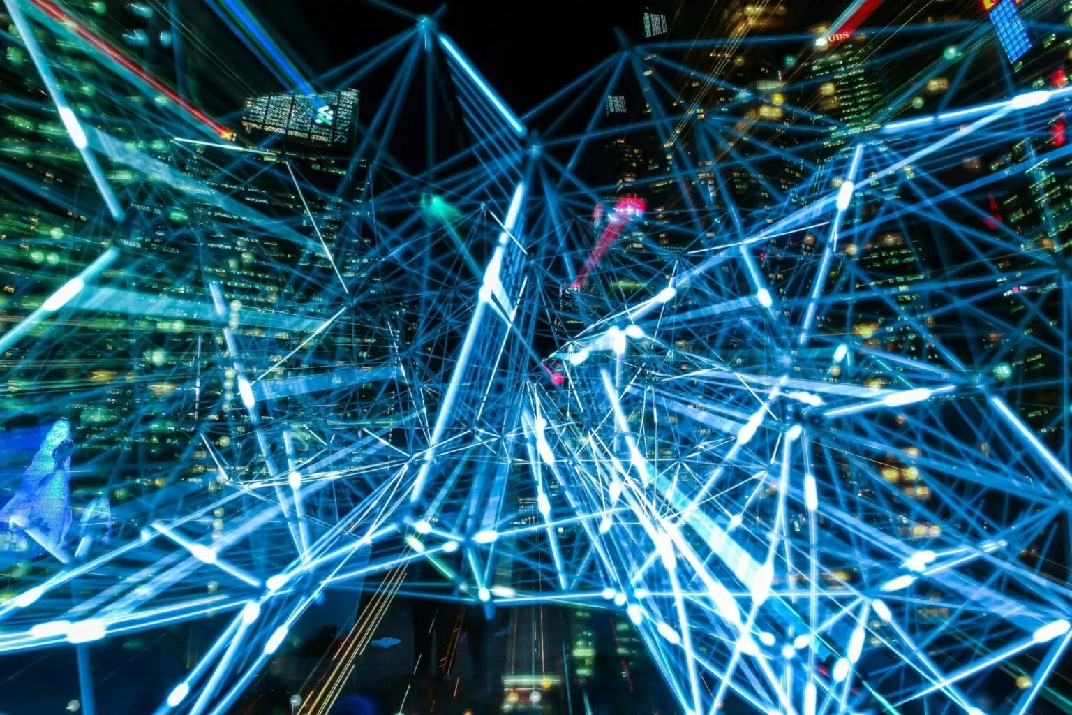 Long-exposure night view of glowing blue light lines forming a web over illuminated skyscrapers