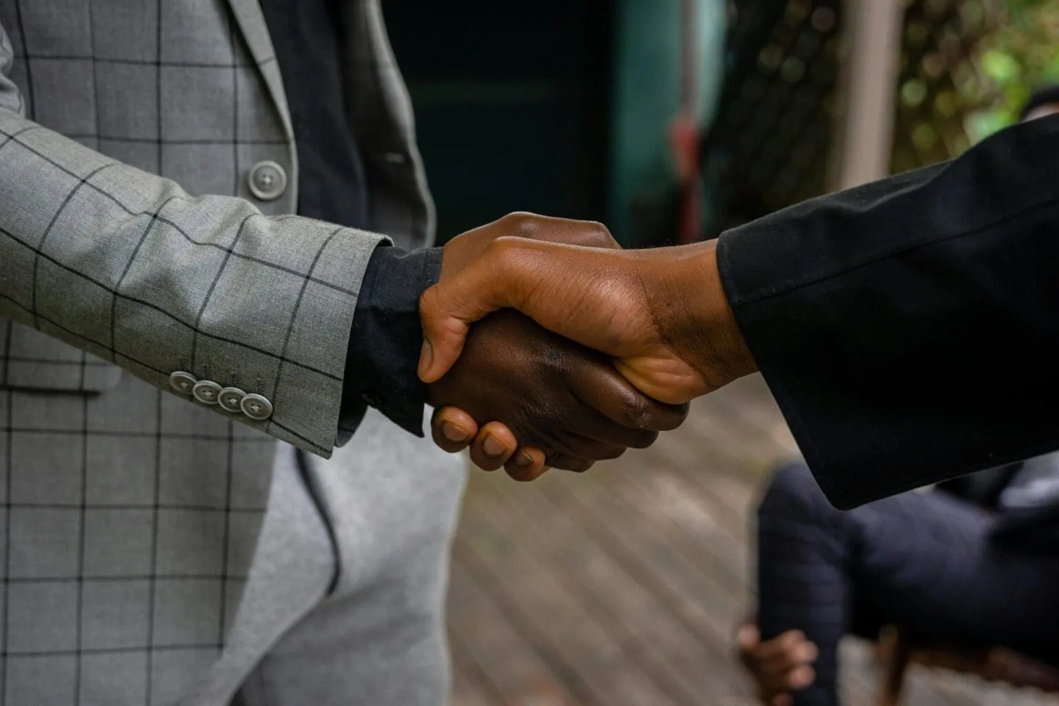 Close-up of two hands clasped in a handshake, one sleeve a gray checked suit jacket