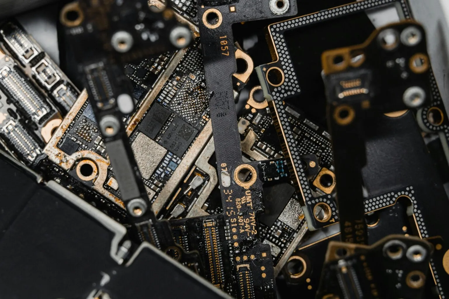 Close-up pile of dark circuit boards with gold-ringed screw holes, connectors and small chips