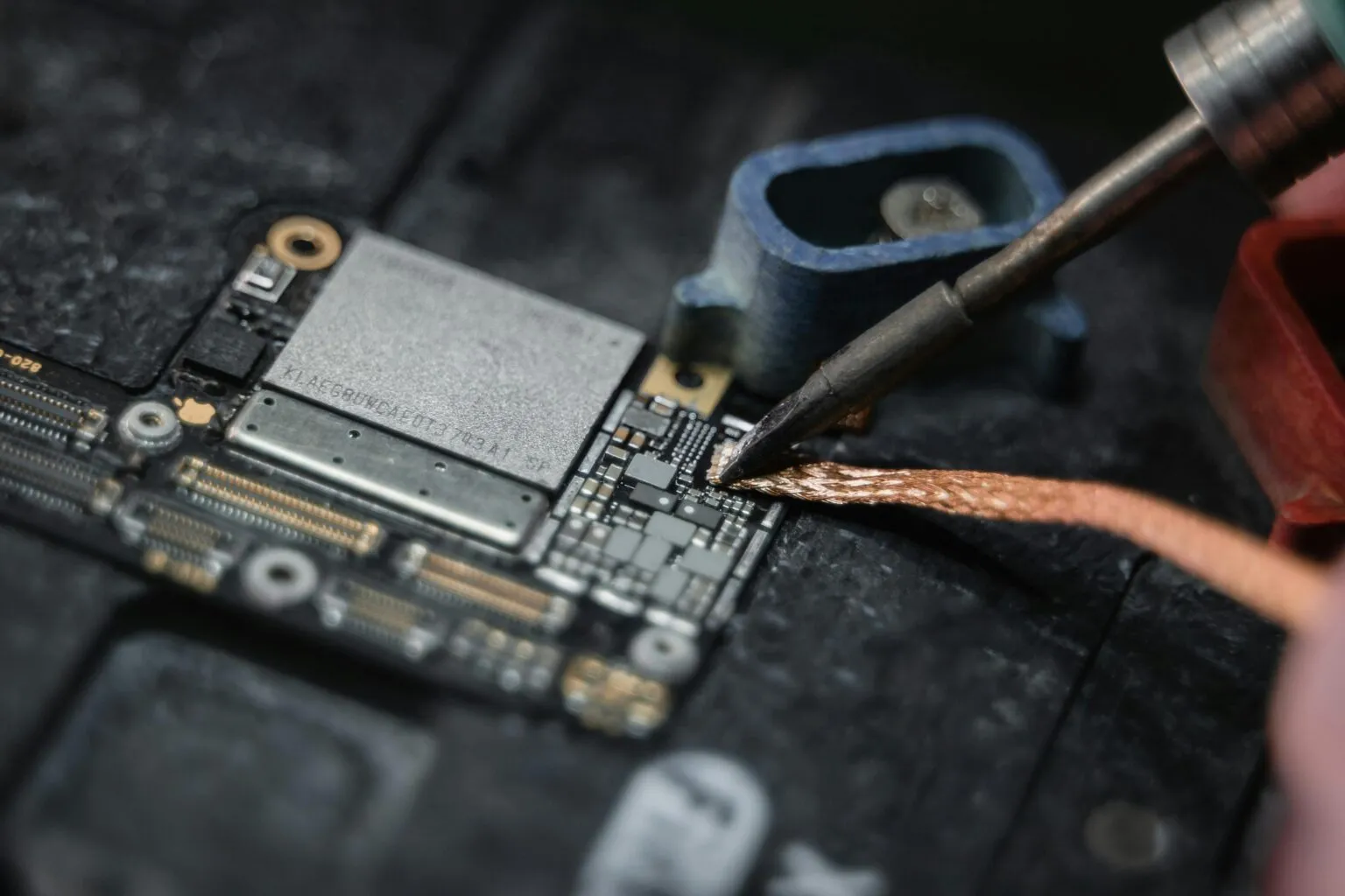 Close-up of a soldering iron tip and copper desoldering braid working on a small component area of a circuit board
